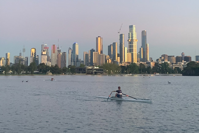 Men rowing on albert park lake, with Melbourne CBD in the background