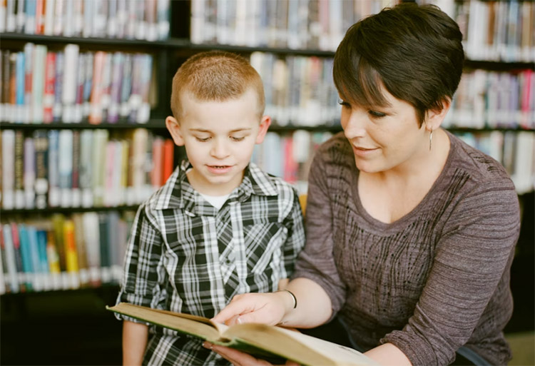 a mother a son sitting together reading a book in a library