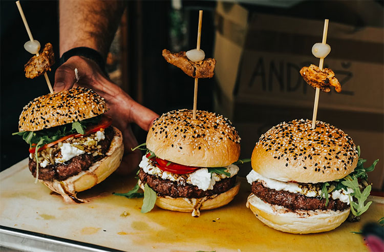 three burgers sitting in a row on a bench