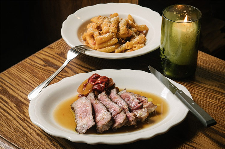 two meals sitting on a dining table beside a candle at albertos loungetwo meals sitting on a dining table beside a candle at albertos lounge