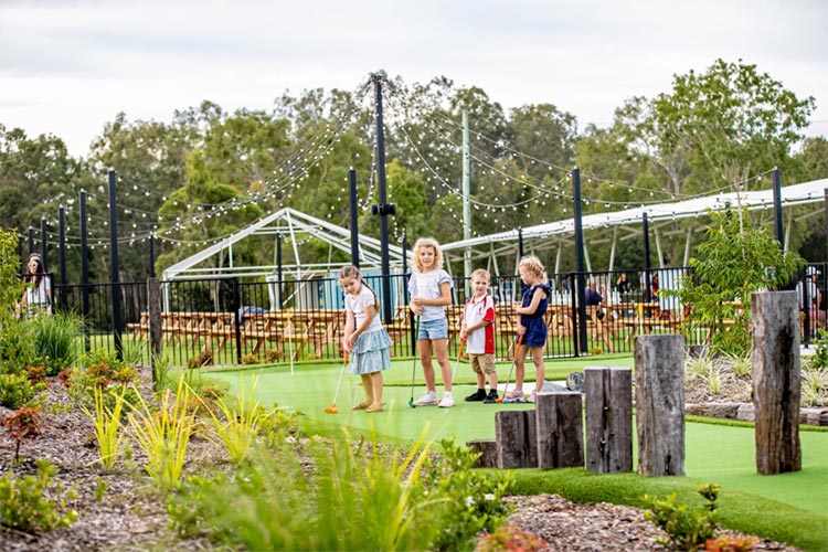 four kids standing on a mini golf lining up to take their shot