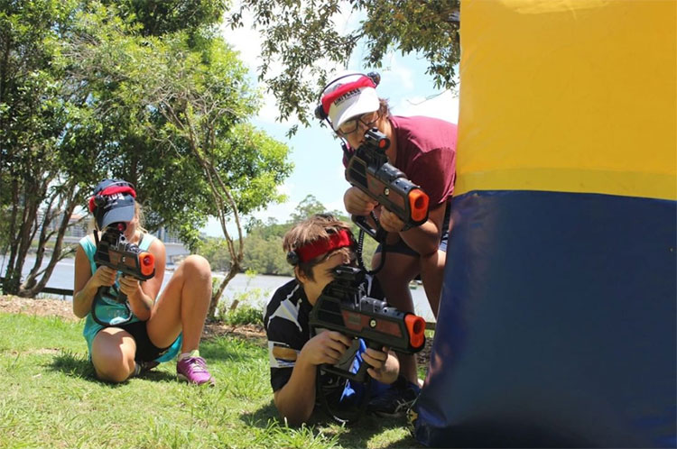 three people standing in a field holding up laser tag guns getting ready to shoot