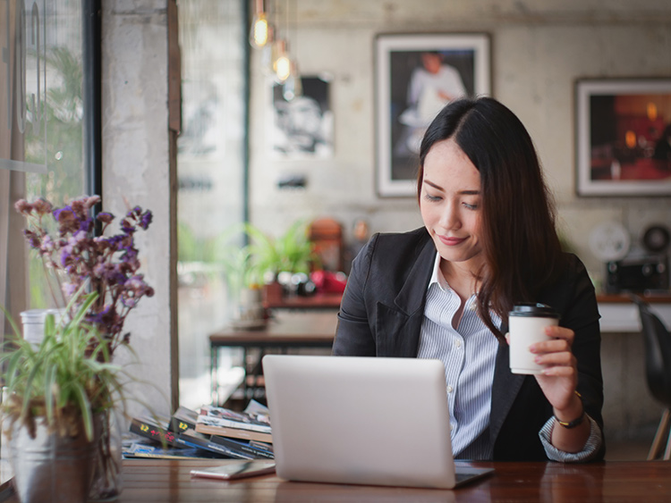 a woman sitting at a table with a coffee in her hand sitting in front of a laptop