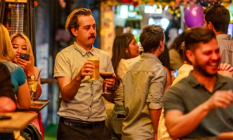 a man holding a beer in a crowd of people in a melbourne bar