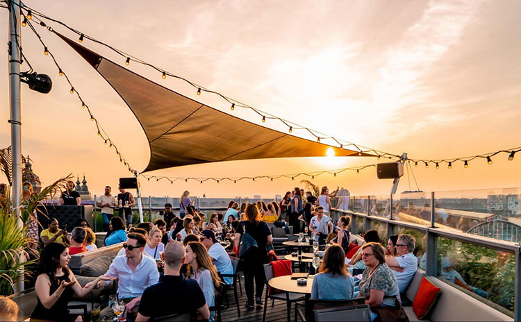 a rooftop bar in melbourne filled with people with views of the sunset