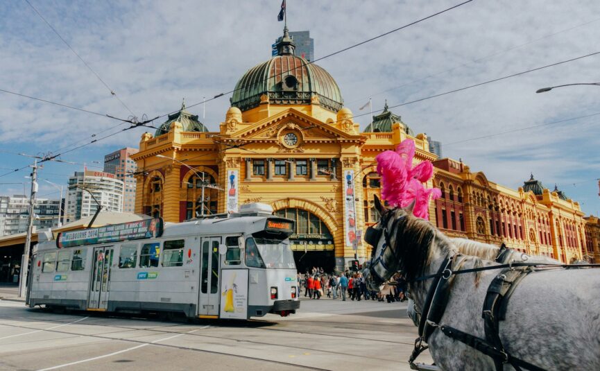 Flinder street during day time; tram and horse passes by